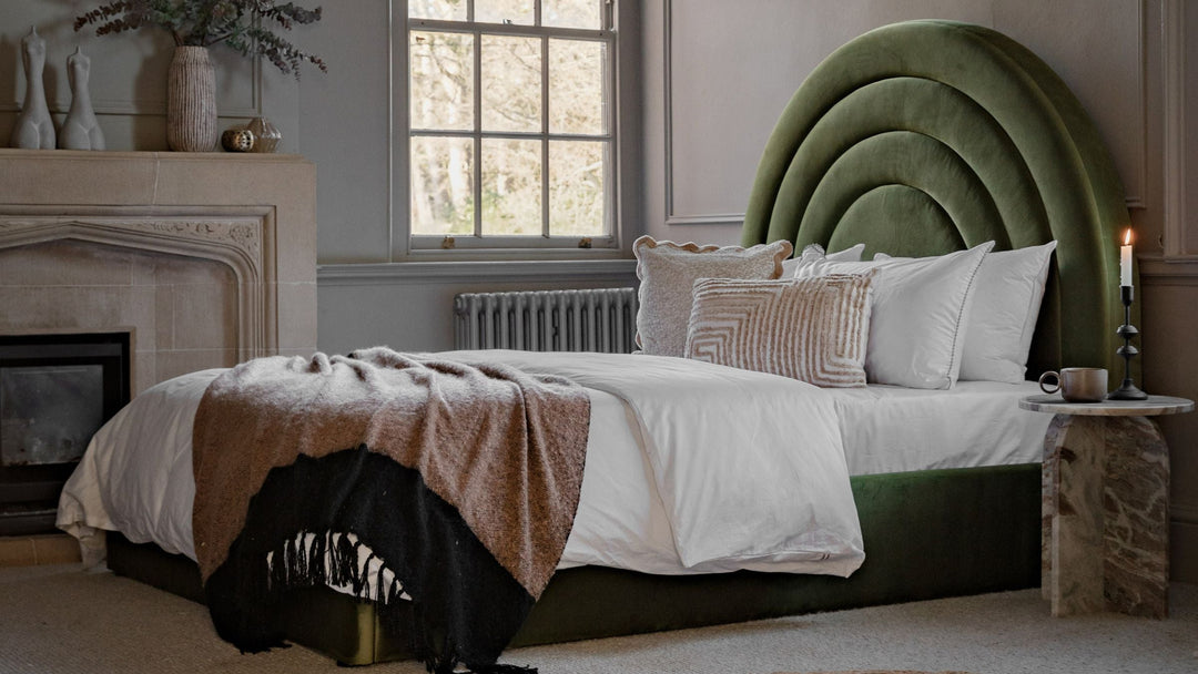 Bedroom setting with green velvet bed covered in cushions and a throw