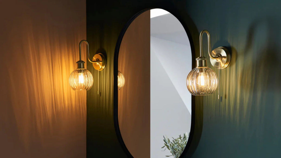 Image of dark green bathroom with two decorative wall lights turned on either side of an oval mirror
