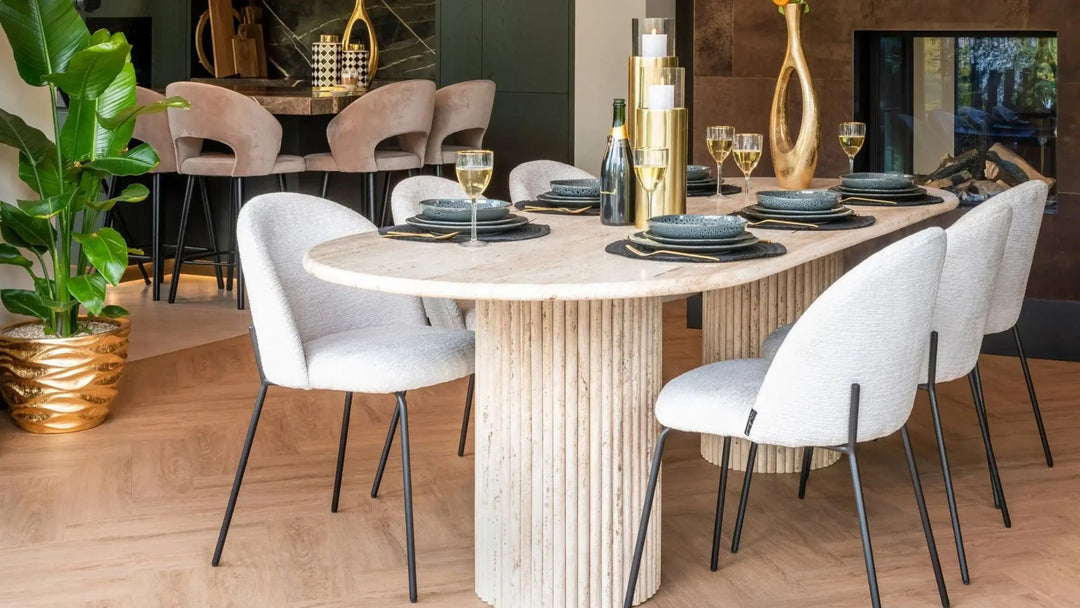6 white dining chairs with black legs around a beige marble dining table with blue plates and gold table settings
