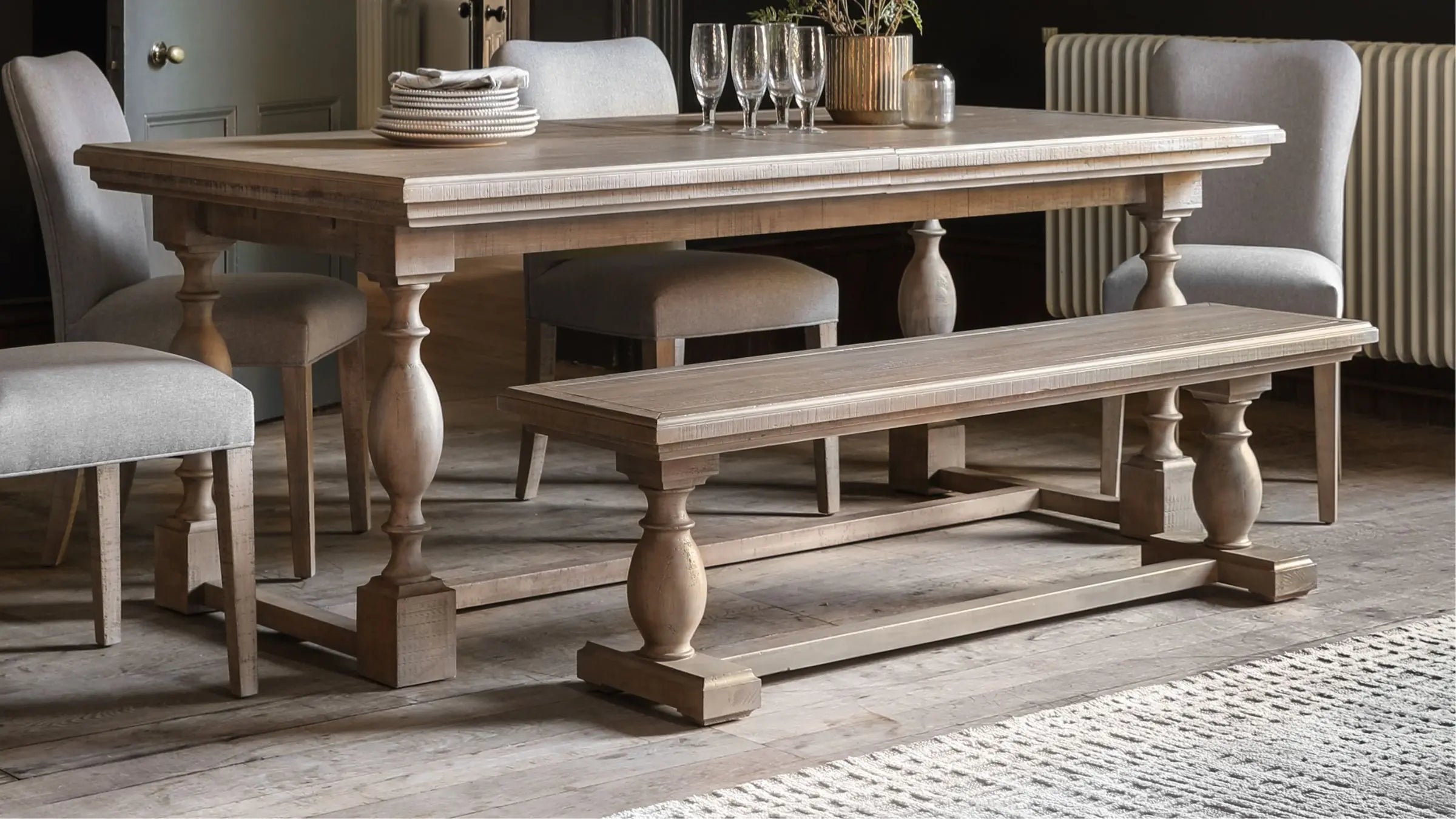 Wooden dining table with glasses and stacked plates with 4 matching dining chairs and dining bench 