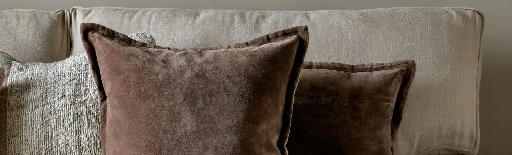 Multiple cushions scattered on a sofa in various shades of blush, pink, neutral and cream