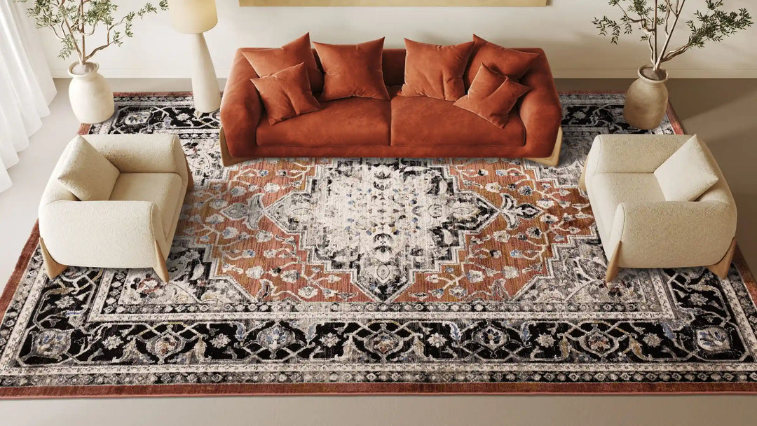 Aerial shot of a living room space with a large patterned rug in the centre, two cream armchairs either end and a rust sofa in the centre with faux plants in stone vases and a cream floor lamp
