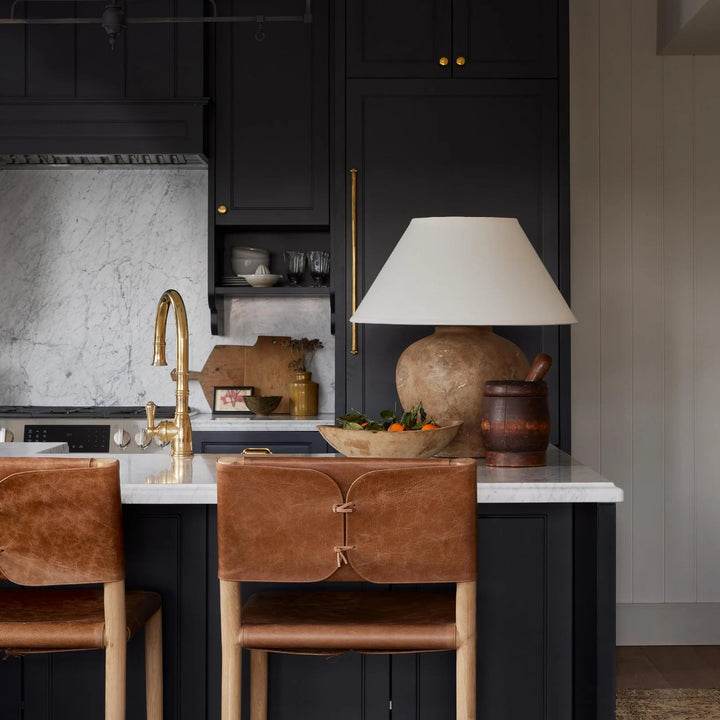 Modern kitchen with black cabinets, marble countertop, and brown leather bar stools.