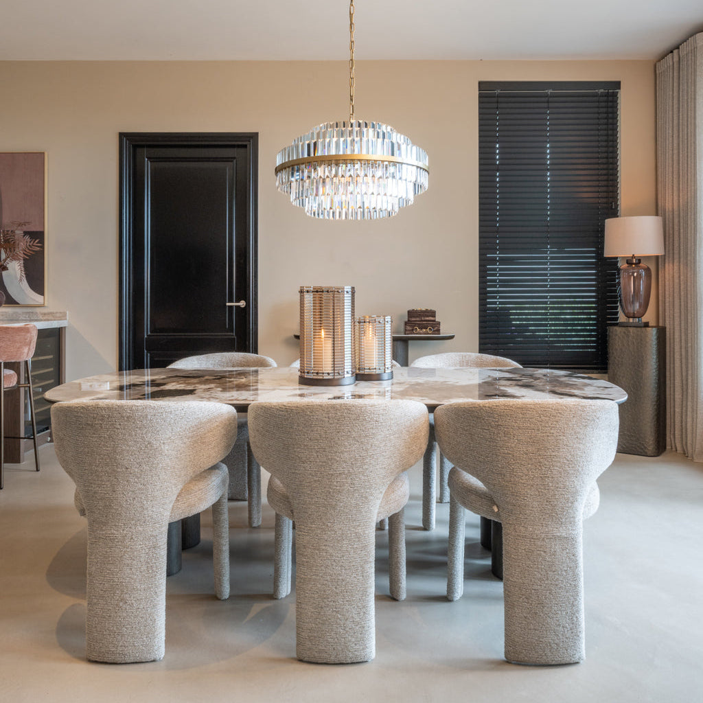 Modern dining room with a round glass table and textured chairs, featuring a chandelier and candles.