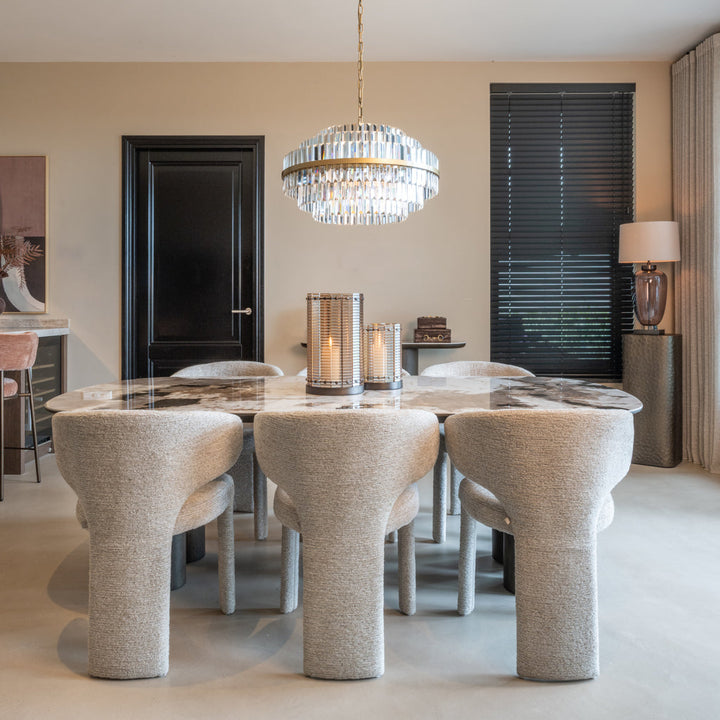 Modern dining room with a round glass table and textured chairs, featuring a chandelier and candles.