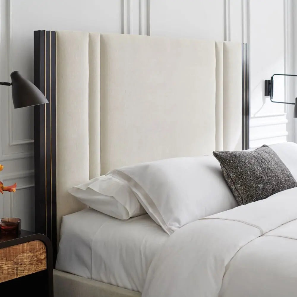 Neatly made bed with white bedding and a decorative pillow against a neutral headboard.