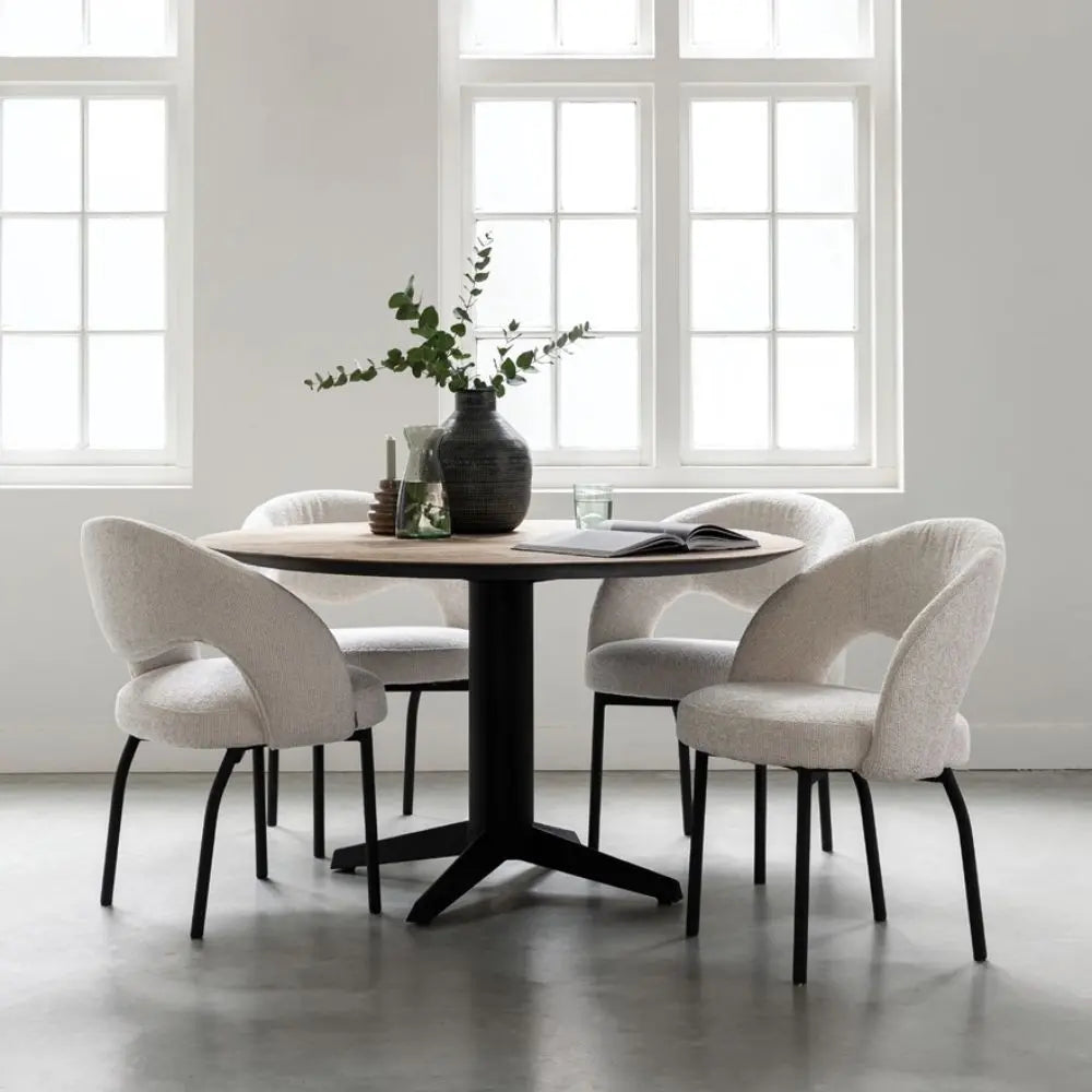 Light, airy dining room setting with wooden and black round dining table and white fabric chairs. 