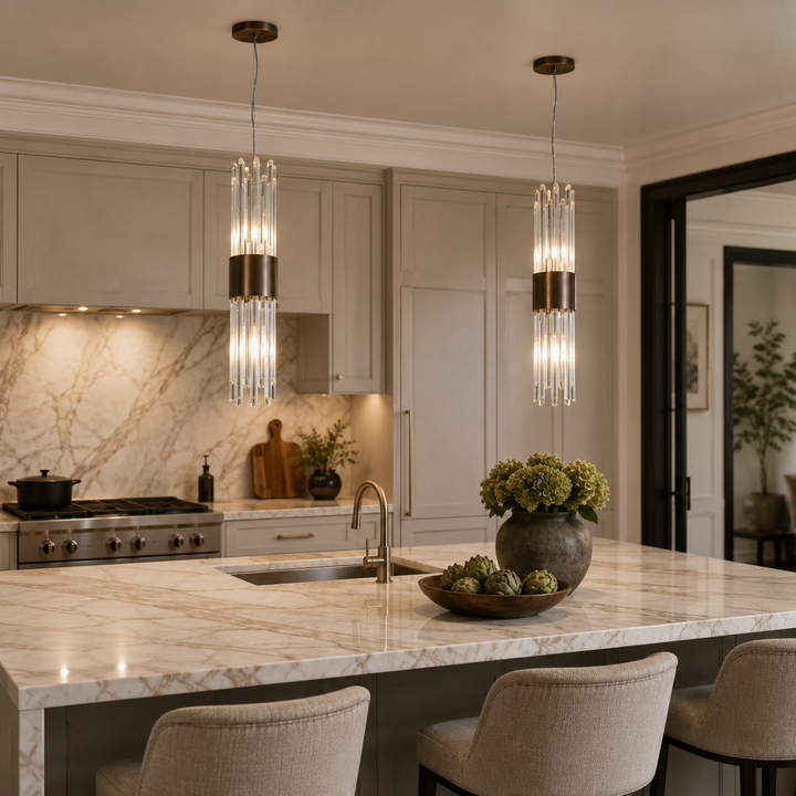 Two modern cylindrical pendant lights with clear glass tubes and brushed brass accents hang over a marble kitchen island in a bright, contemporary kitchen.