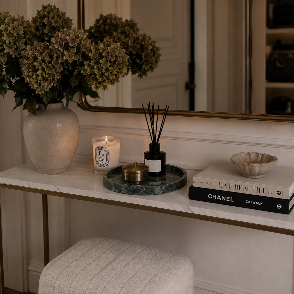 A styled interior console table scene with a large beige vase of dried flowers, a lit candle, a dark reed diffuser on a green marble tray, a small bowl, a Chanel and Livestreaming book, and a mirror above. No person is present, but this is a real environment rather than a clean isolated product shot, so subject_type is Lifestyle.