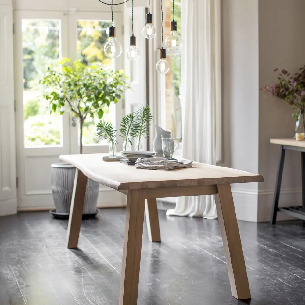 Scandi style oak dining table placed on dark black wooden flooring with industrial style lights. 