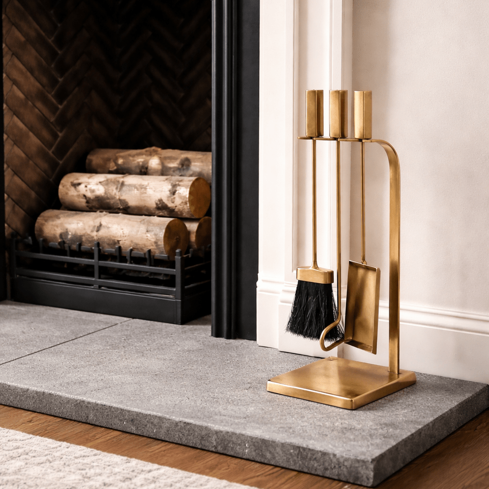 Gold fireplace tools set against a white wall with a fireplace.