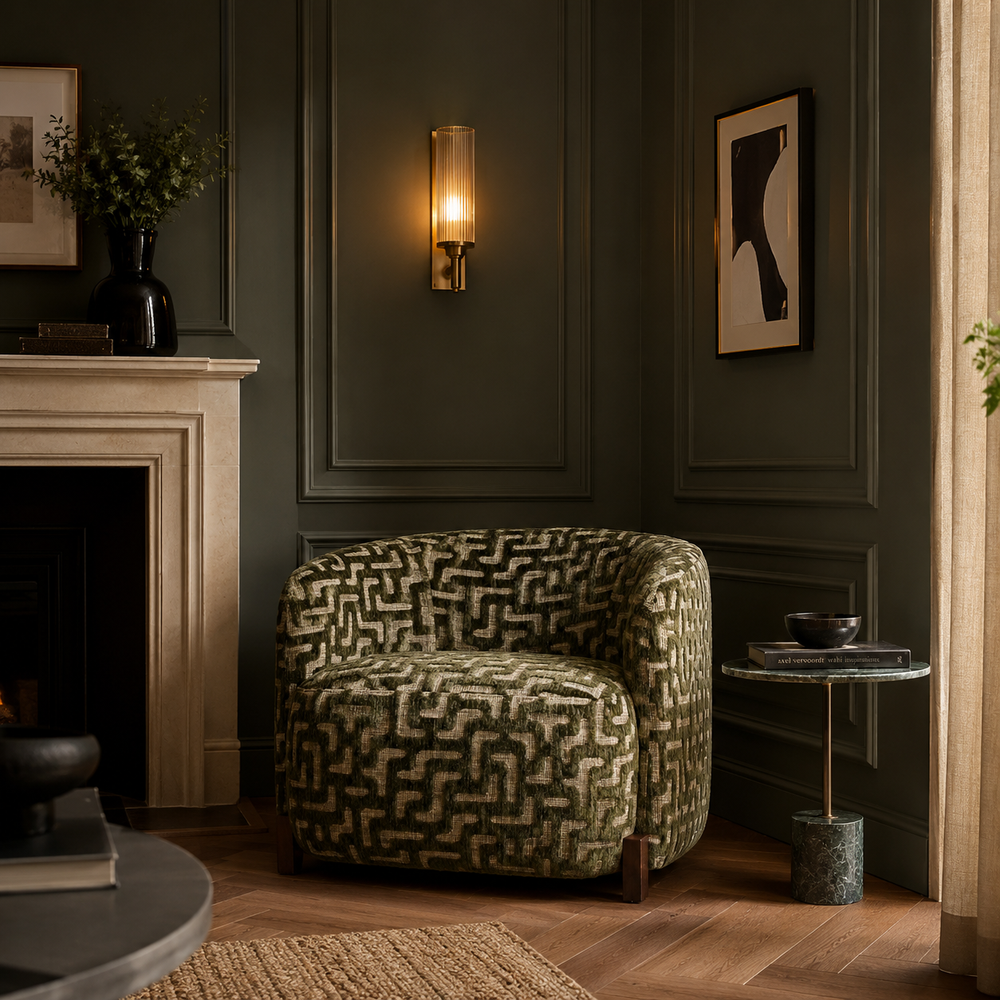 A patterned armchair in a dark green and beige geometric design, placed in a styled living room with a fireplace, wall sconce, and side table.