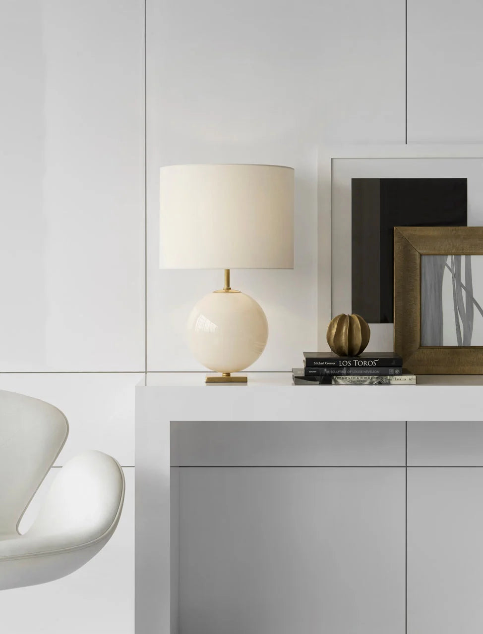 Modern interior with a lamp, books, and decorative items on a shelf against a light gray wall.