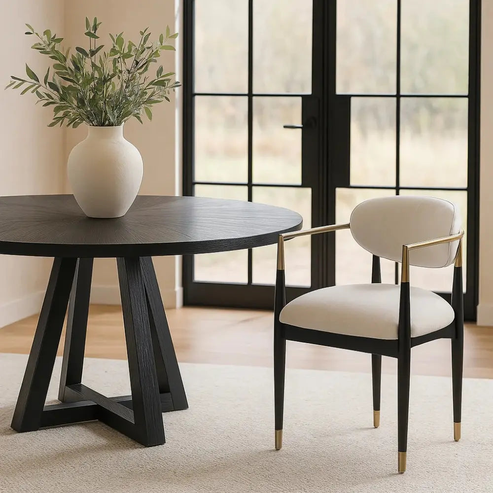 Dining table with a vase of greenery and a chair in a room with large windows.