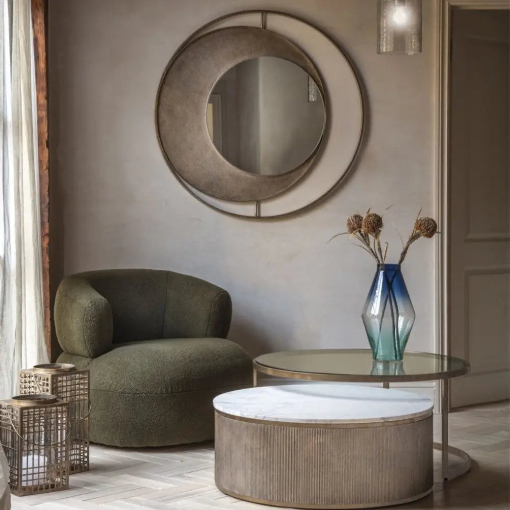 Modern interior with a green armchair, round mirror, and glass coffee table.