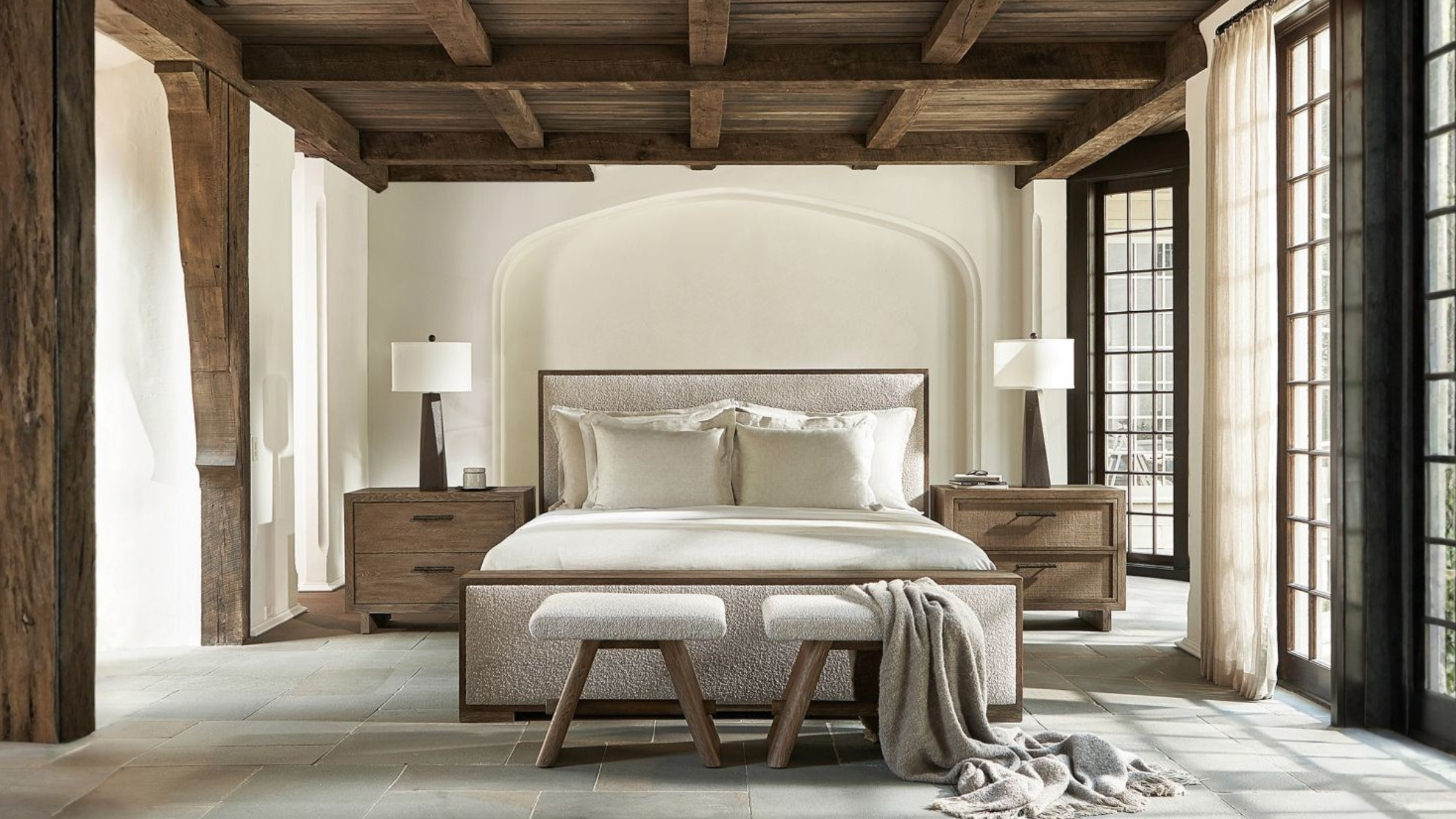 Modern bedroom with wooden beams, large windows, and a bed with pillows.