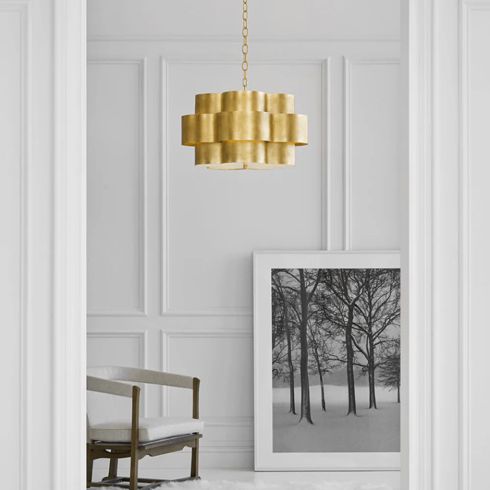 Gold pendant light fixture hanging above a framed photograph of trees in a snowy landscape on a white paneled wall.