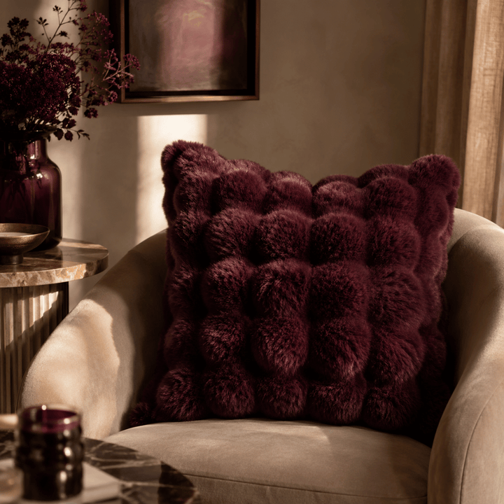 Fluffy purple pillow on a beige armchair in a cozy room.