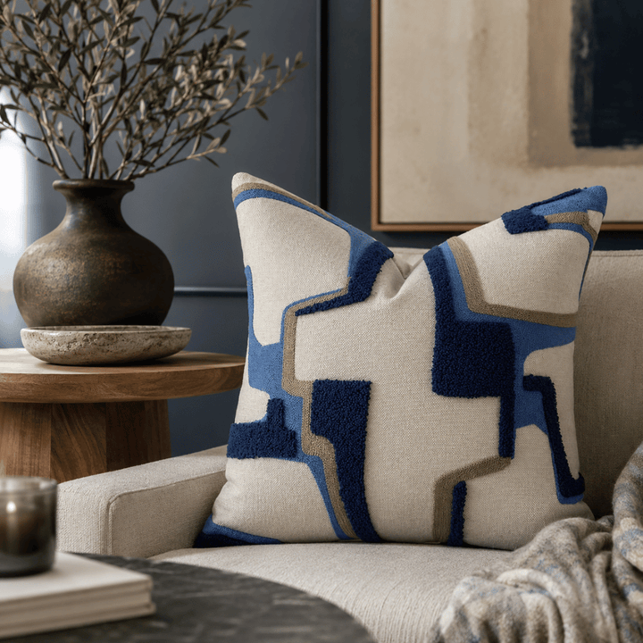 Decorative pillow with geometric pattern on a couch, next to a wooden side table with a vase.
