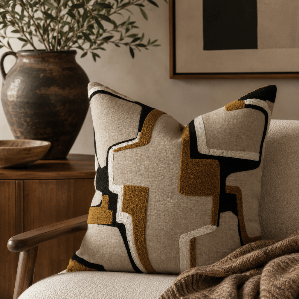 Decorative pillow with geometric pattern on a chair, with a vase and plant in the background.