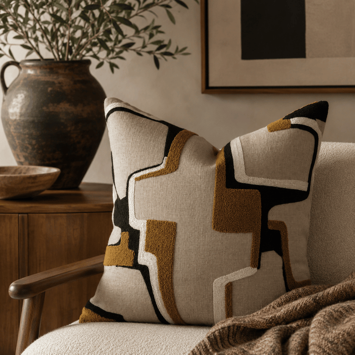 Decorative pillow with geometric pattern on a chair, with a vase and plant in the background.
