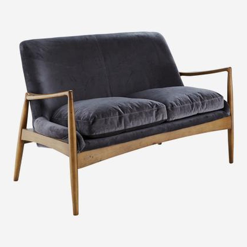 A sumptuous grey velvet sofa in a dark rich wooden frame. Crispin displays a mid-century silhouette with thin arms and legs naturally decorated with wood graining.