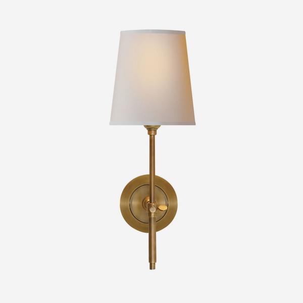 A small wall lamp in hand-rubbed antique brass with a plain natural shade. 